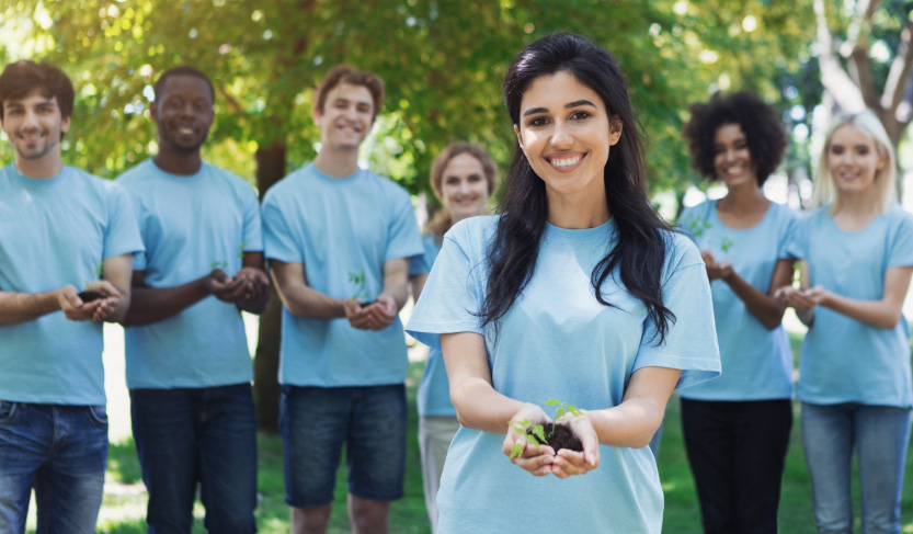 ”Young volunteers in blue t-shirts enjoying planting trees together.”
